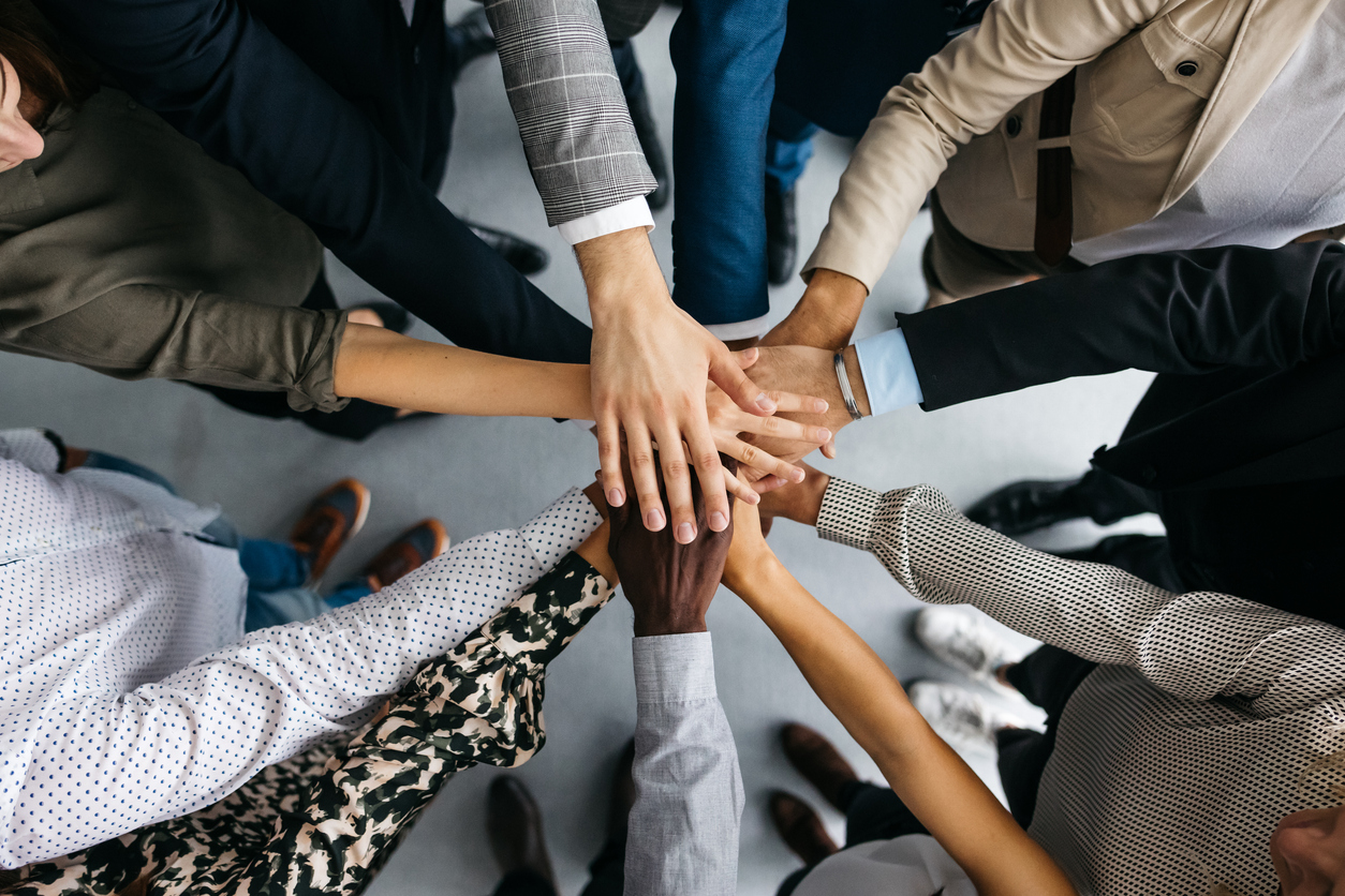 Close-up of co-workers stacking their hands together Alchemy Mentoring Leadership - Coming Together